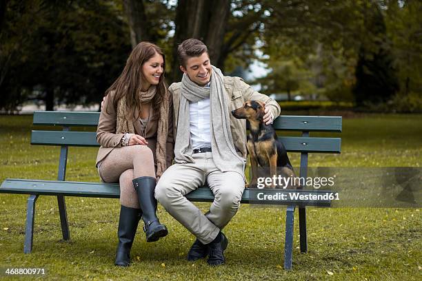 happy couple with dog in a park - woman dog bench stock pictures, royalty-free photos & images