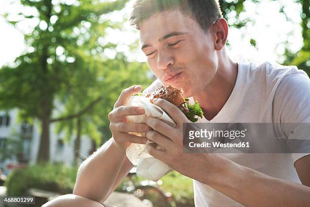 young man eating hamburger - snacking on the go stock-fotos und bilder