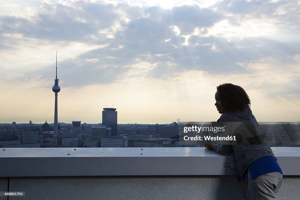 Germany, Berlin, Young woman on rooftop terrace, looking at view