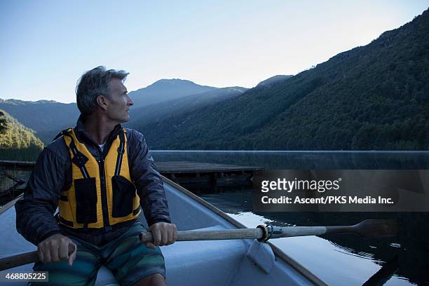 man rows boat across tranquil lake, dawn - life jacket stock pictures, royalty-free photos & images