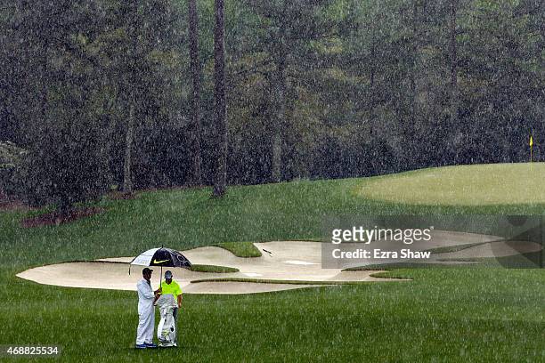 Rory McIlroy of Northern Ireland waits with his caddie J.P. Fitzgerald in the rain during a practice round prior to the start of the 2015 Masters...