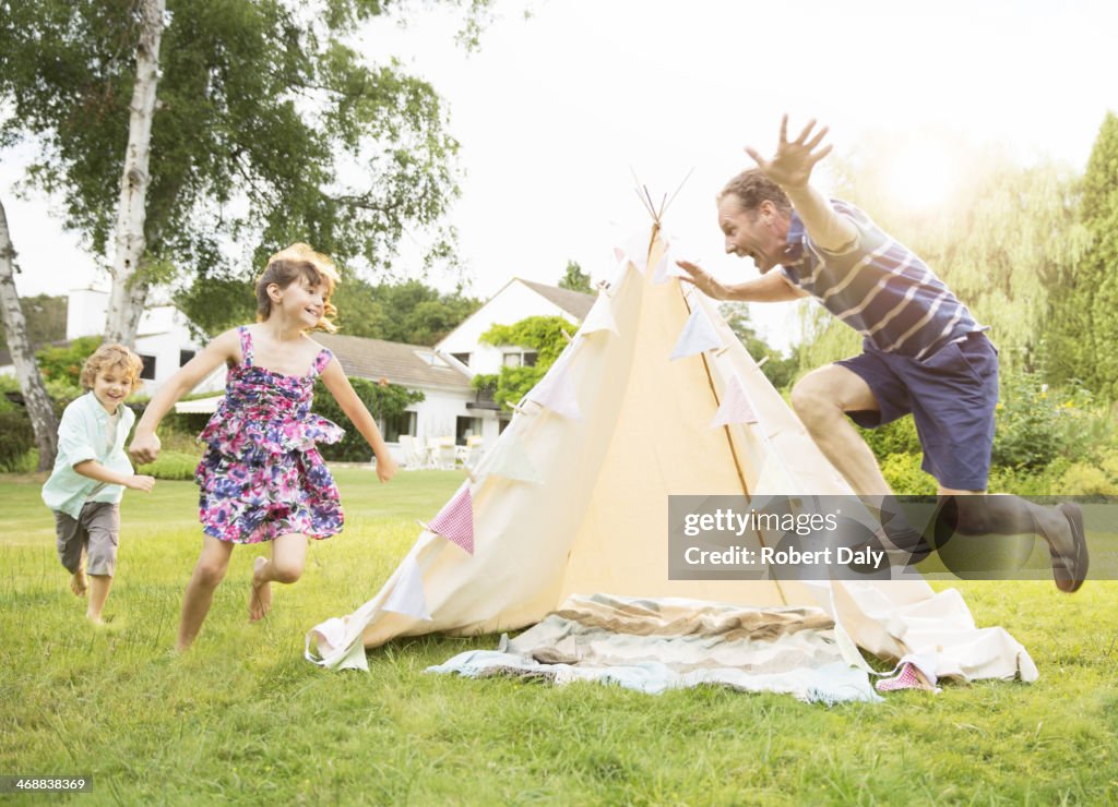 Father chasing children around teepee in backyard