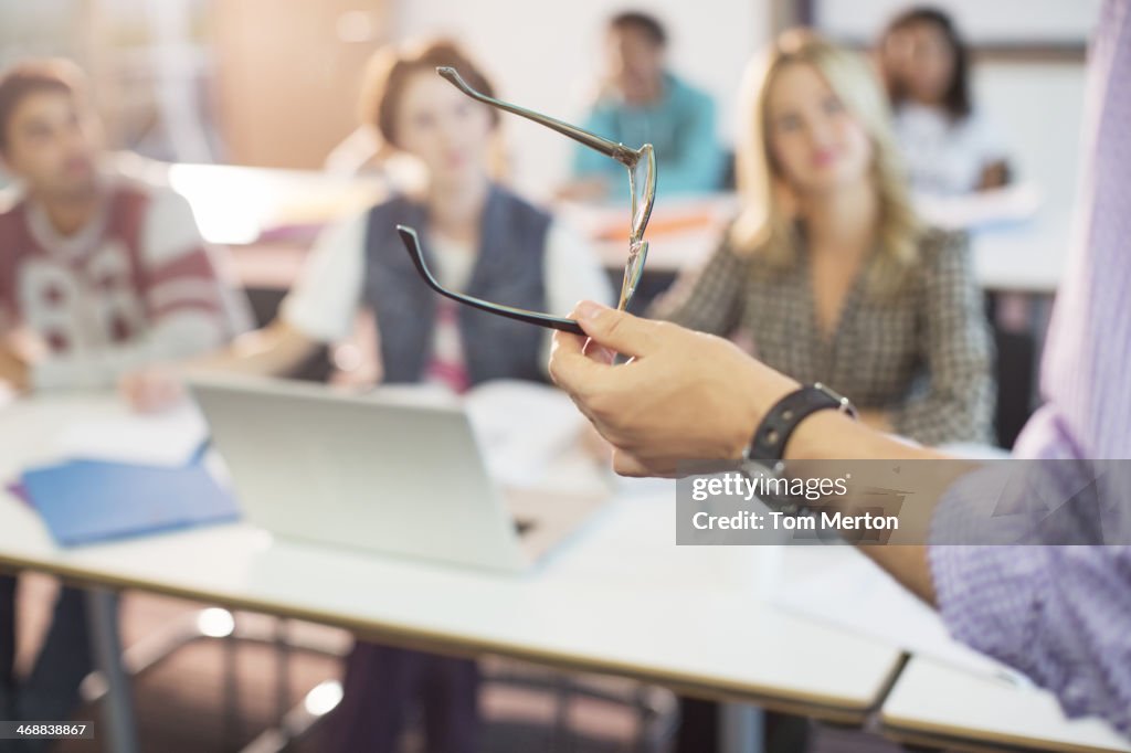 Professor gesturing with eyeglasses in classroom