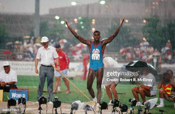 American track and field athlete Carl Lewis raises his arms in the rain on the field of Indiana-Purdue University Stadium during at the US Olympic...