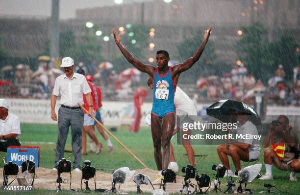 American track and field athlete Carl Lewis raises his arms in the rain on the field of Indiana-Purdue University Stadium during at the US Olympic...