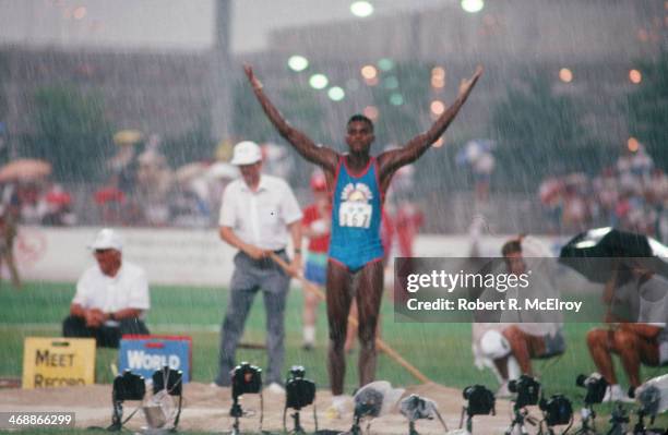 American track and field athlete Carl Lewis raises his arms in the rain on the field of Indiana-Purdue University Stadium during at the US Olympic...