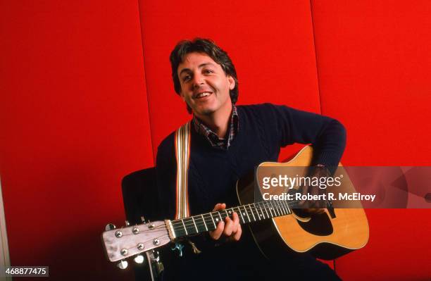 Portrait of British musician Paul McCartney as he plays acoustic guitar against a red background, October 7, 1984 .