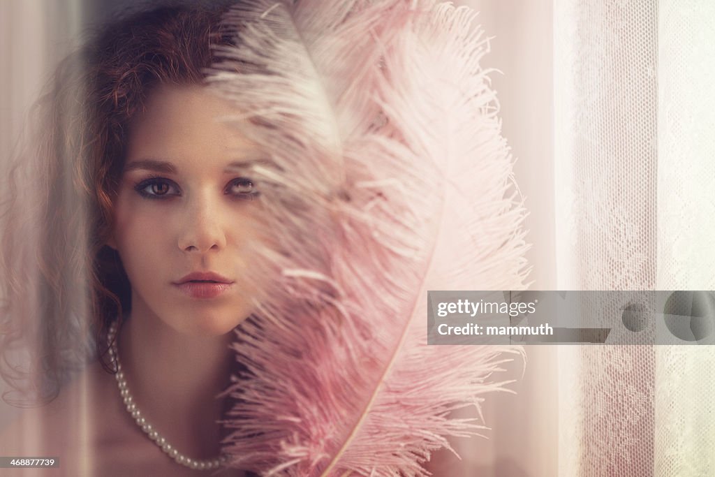 Young girl with feather fan by the window