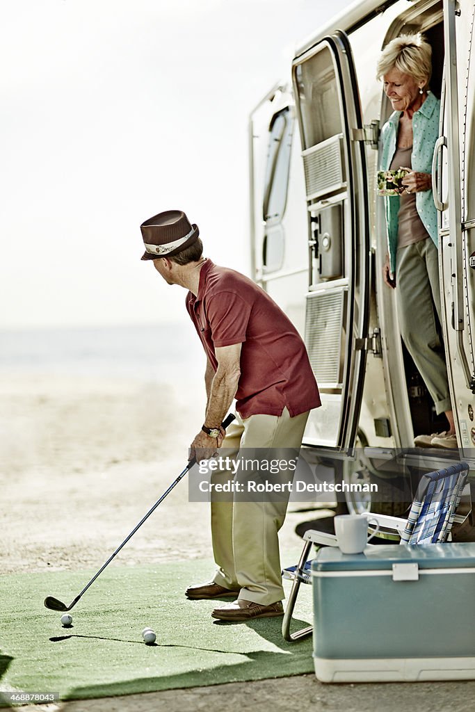 A man playing golf while a woman watches on.