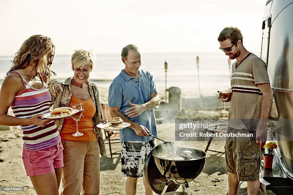 A group of people talking and laughing near a BBQ.