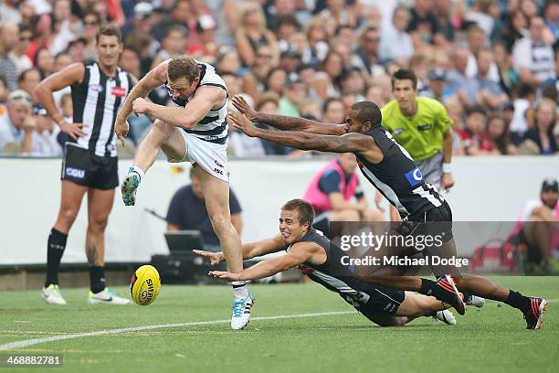 Steven Johnson of the Cats kicks the ball away from Ben Kennedy and Heritier Lumumba of the Magpies during the round one AFL NAB Cup match between...