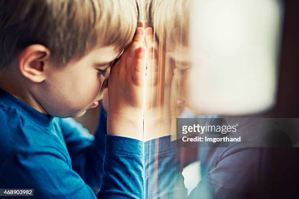 sad little boy leaning aganing the window - orphan boy stock pictures, royalty-free photos & images