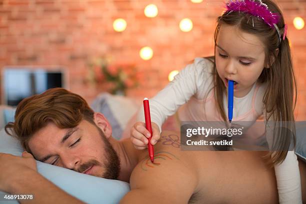 cute daughter drawing on her sleeping father's back. - tiara drawing stock pictures, royalty-free photos & images