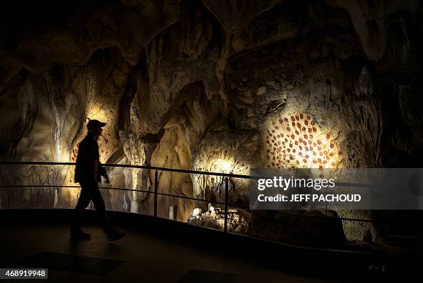 Person walks past the full-scale reproduction of frescos found at the cave of Pont-D'Arc also known as the Chauvet cave, on April 8, 2015 in Vallon...
