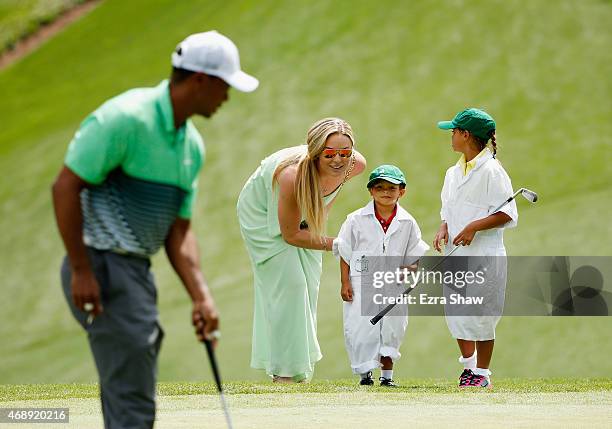 Tiger Woods of the United States walks across a green as his girlfriend Lindsey Vonn, son Charlie and daughter Sam look on during the Par 3 Contest...