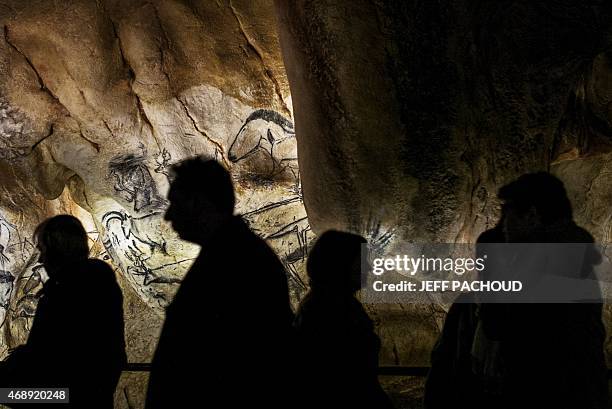 People walks past the full-scale reproduction of frescos found at the cave of Pont-D'Arc also known as the Chauvet cave, on April 8, 2015 in Vallon...