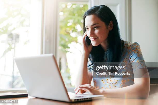 woman using laptop whilst talking on smart phone. - using phone and laptop stock pictures, royalty-free photos & images