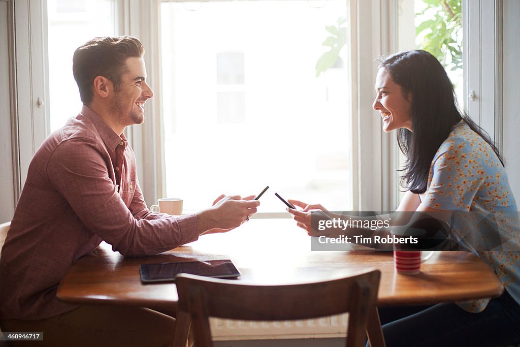 Man and woman using smart phones at table.