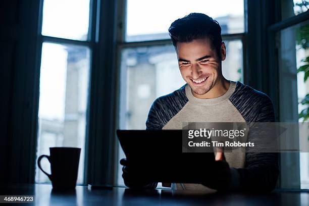 man at table lit by digital tablet. - excitement computer stock pictures, royalty-free photos & images