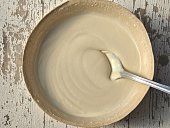 A spoon in bowl of creamy tahini, on a wooden table
