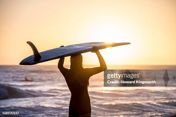 female surfer at sunrise standing on beach - woman surfboard stockfoto's en -beelden