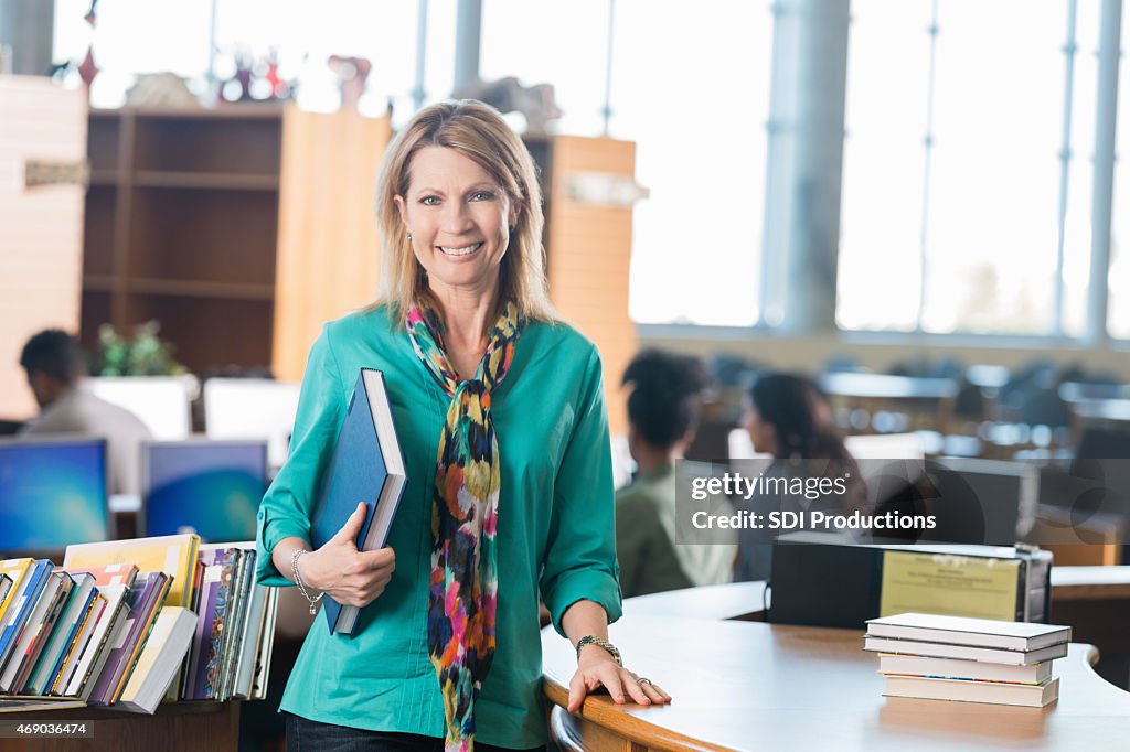 Mature teacher standing at library check-out desk