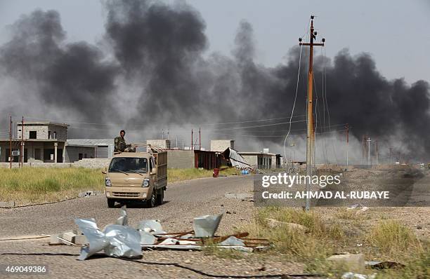 Members of the pro-government forces drive in front of smoke billowing from what is believed to be an oil field which was set alight by Islamic State...