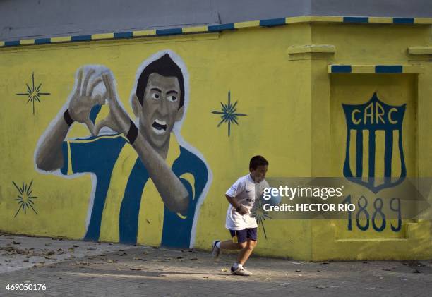 Kid holding a ball runs past a mural depicting Argentine footballer Angel Di Maria painted in a corner near the Gigante de Arroyito stadium of...