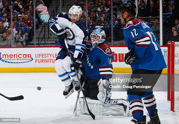 Jim Slater of the Winnipeg Jets leaps to avoid the puck as goalie Reto Berra of the Colorado Avalanche defends the goal against the shot at Pepsi...