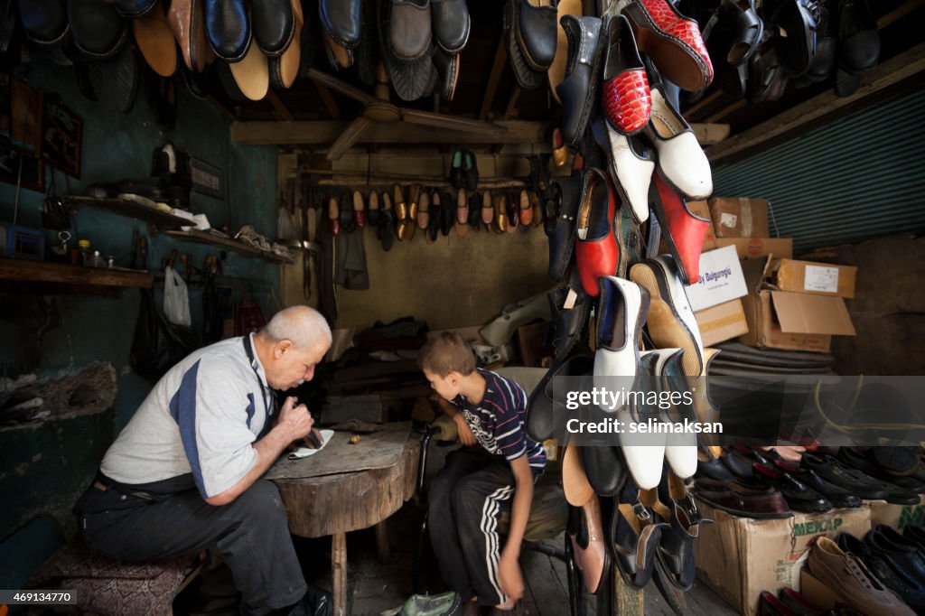 Traditional senior shoemaker teaching his apprentice how to work