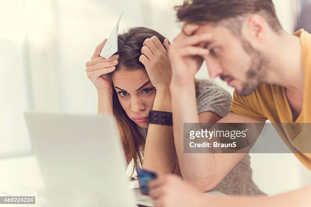 couple in emotional distress staring at laptop screen - credit card debt stockfoto's en -beelden
