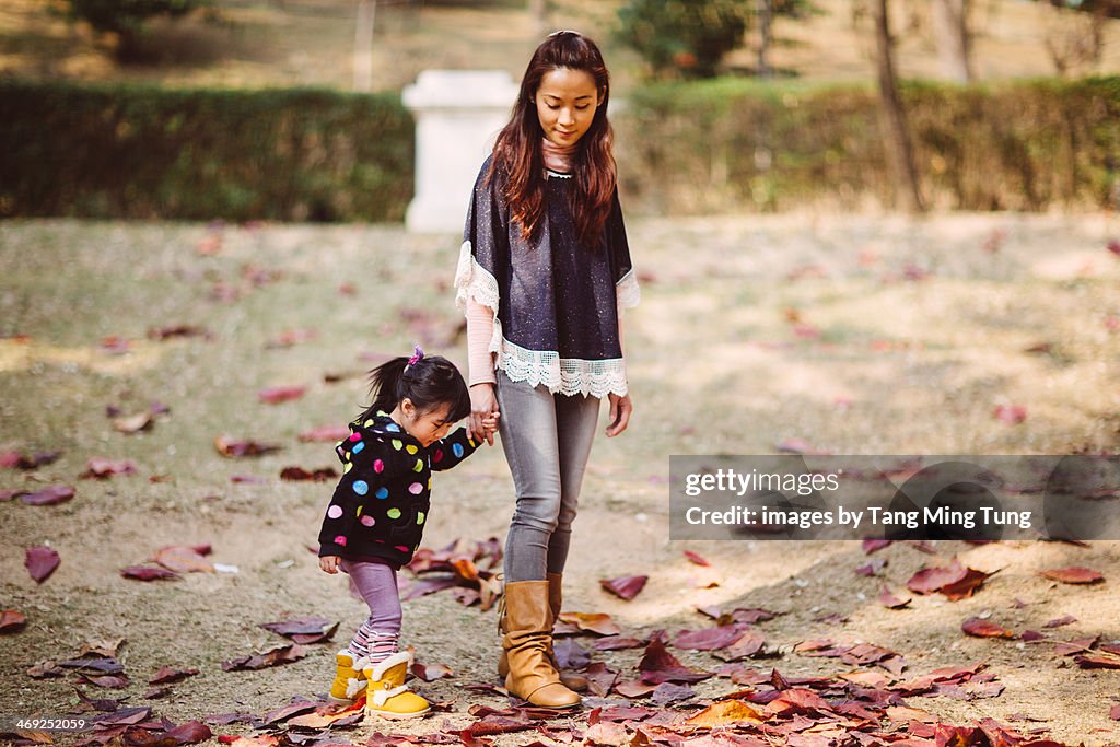 Mom & toddler girl strolling on lawn in park