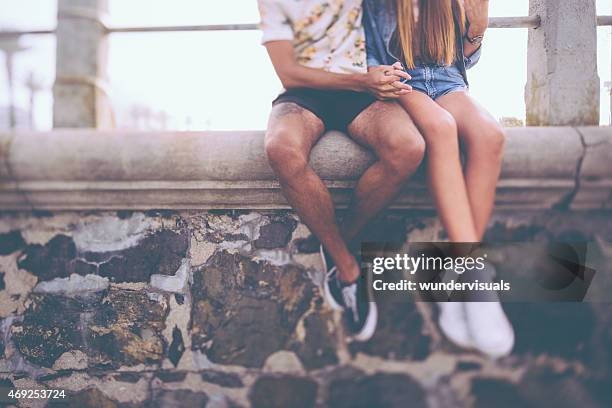 legs of hipster couple sitting on a wall holding hands - teenage romance stock pictures, royalty-free photos & images