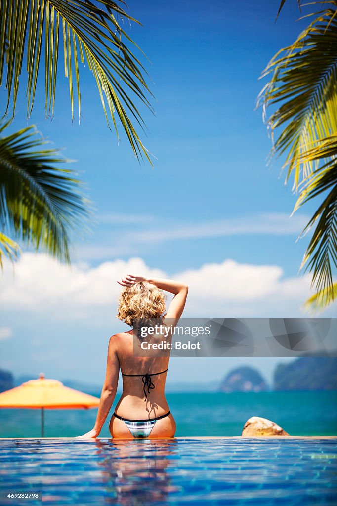 Mujer sentada en el borde de la piscina de borde infinito, Vista posterior