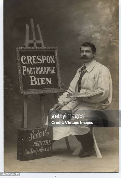 An artist sits by a sign reading 'Crespon Photographie Bien' and another reading 'Sadoul Peintre, Rue Montpellier, 27', circa 1900.