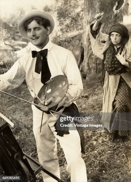 Malevolent gypsy woman creeps up on an unsuspecting artist with a dagger in a scene from a film, circa 1920.