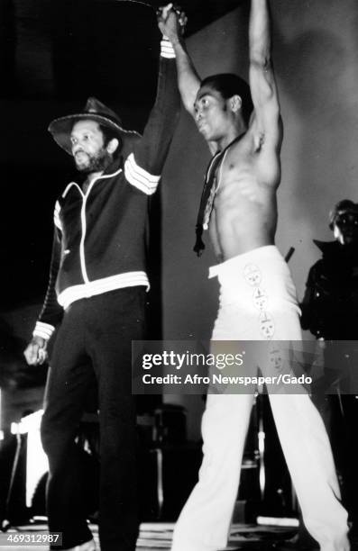 Musicians Roy Ayers and Fela Kuti on stage with arms raised, circa 1986.