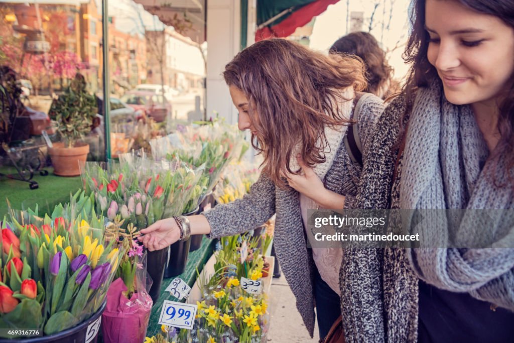 Young women shopping for spring flowers on city sidewalk.