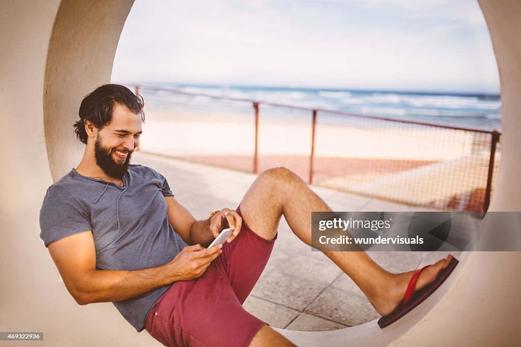 Glücklicher Mann auf seinem Handy am Strand