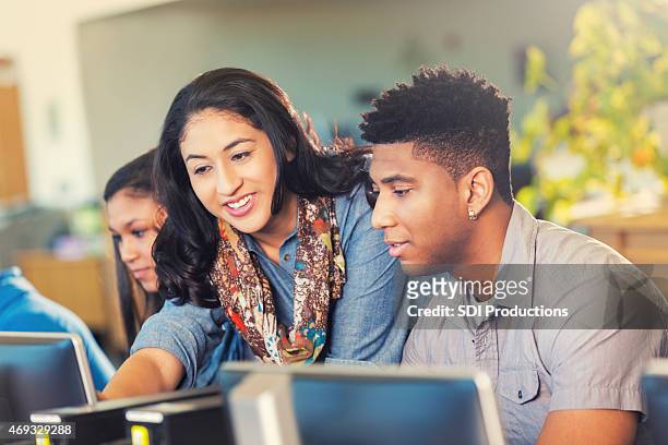 pretty hispano profesor ayudando a adolescente afroamericana con ordenador de la asignación - computer lab fotografías e imágenes de stock