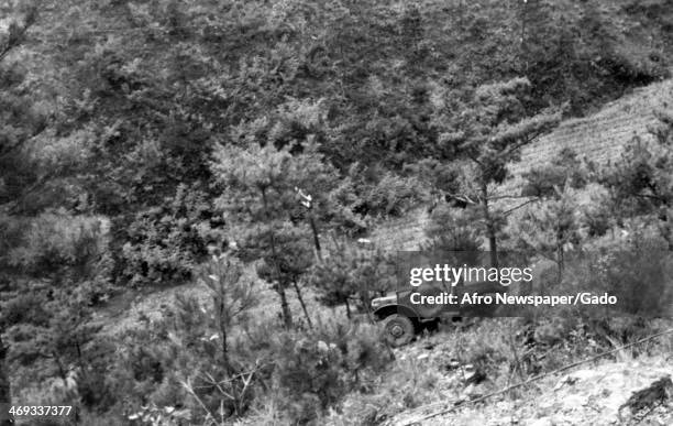 Photograph taken from high on mountain trail showing a weapons carrier that was blown off the road by a land mine during enemy breakthrough of the...