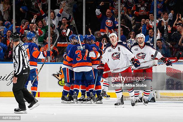 Brandon Dubinsky and Fedor Tyutin of the Columbus Blue Jackets skate away as Kyle Okposo of the New York Islanders is congratulated by his teammates...