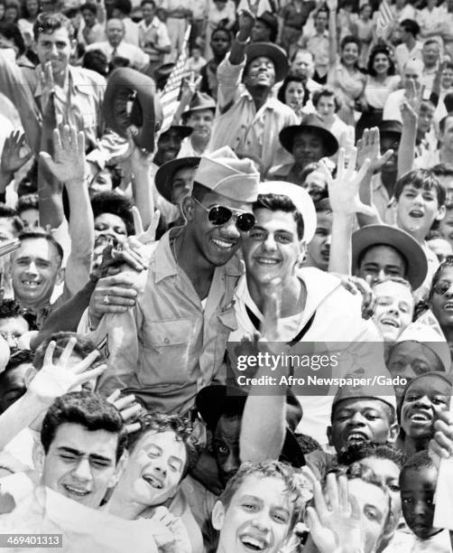 White sailor and an African American soldier hug while being lifted onto the shoulders of a diverse crowd on VJ Day, following the victory over Japan...