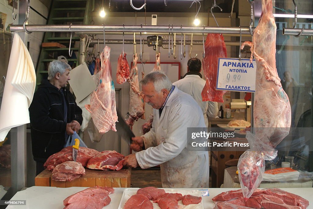Butchers chop meat for customers. Greek people visit the...