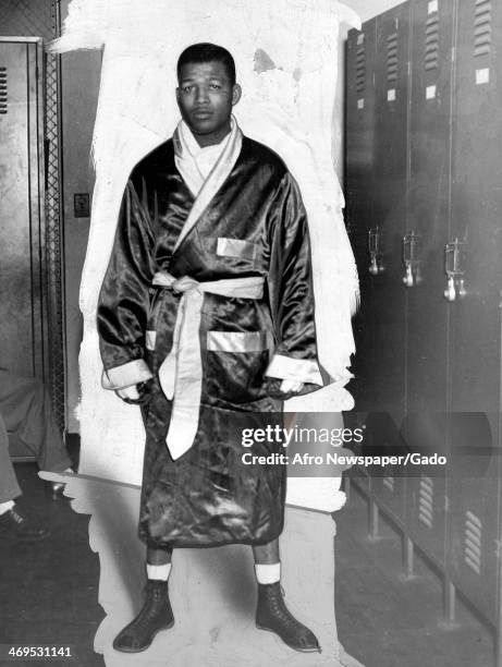 Full length portrait of boxing champion Sugar Ray Robinson standing in a locker room, wearing a boxing robe, gloves and shoes, September 14, 1946.