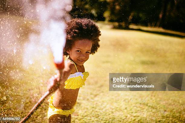 african girl spraying water from garden hose - tuinslang stockfoto's en -beelden