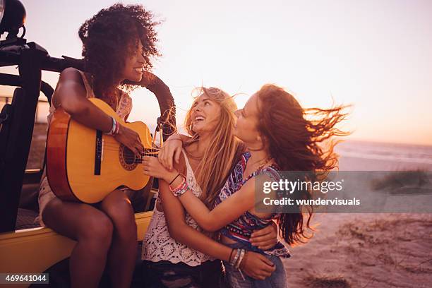 afro mädchen spielt gitarre für ihre freunde bei sonnenuntergang - girl beach sunset stock-fotos und bilder