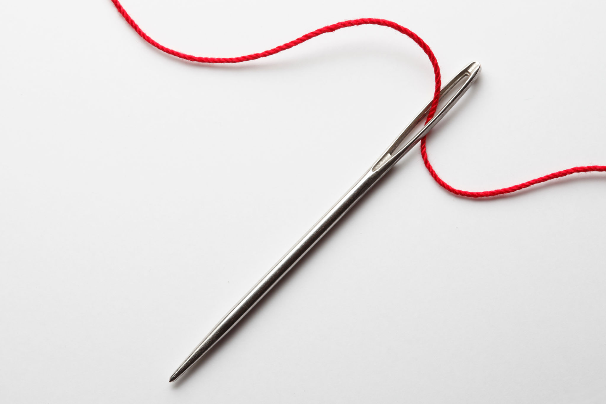 Close up of threading eye of a needle with red thread Close up of threading eye of a needle with red thread