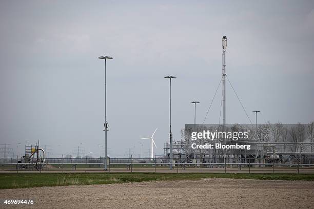 Wind turbine and electricity transmission pylons stand beyond natural gas extraction machinery and pipework on an onshore site operated by...