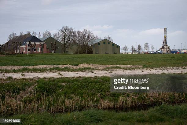 Gas drilling rig, right, stands on an onshore extraction site operated by Nederlandse Aardolie Maatschappij BV beside farm buildings on the Loppersum...